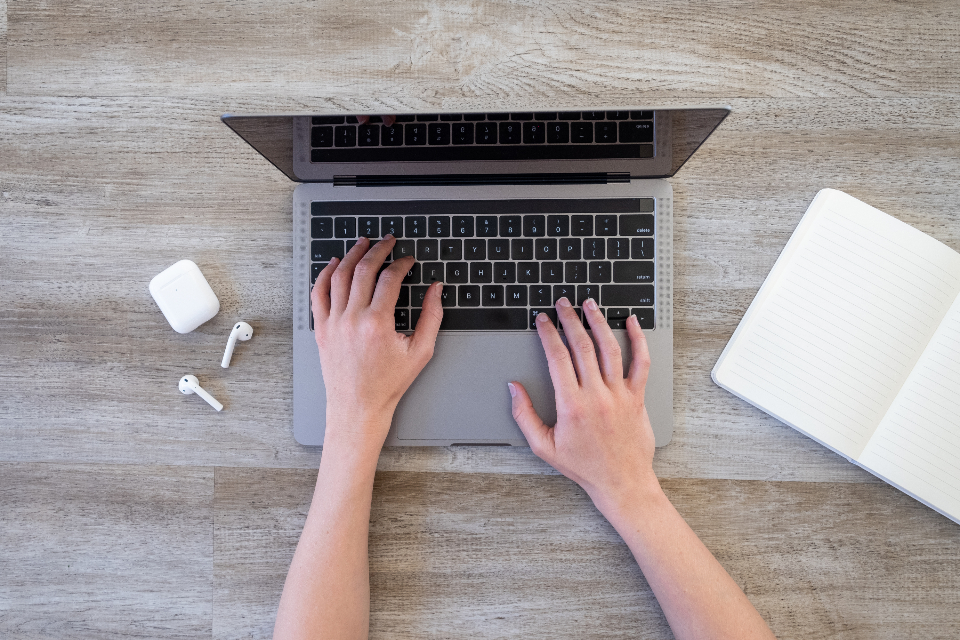Persona escribiendo en laptop junto a un cuaderno de notas